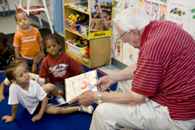 Seated man reads a book to children in a classroom