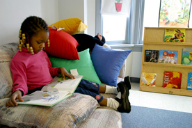 Young girl sits on couch and looks at book in her lap