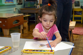 Young girl painting on paper while seated at desk