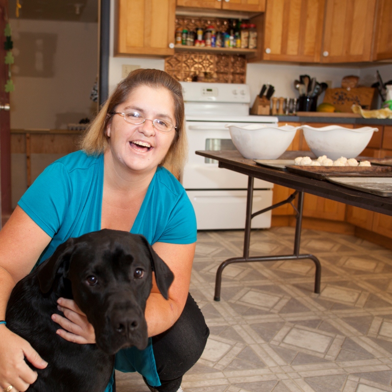 Woman hugs black lab in kitchen and smiles for the camera