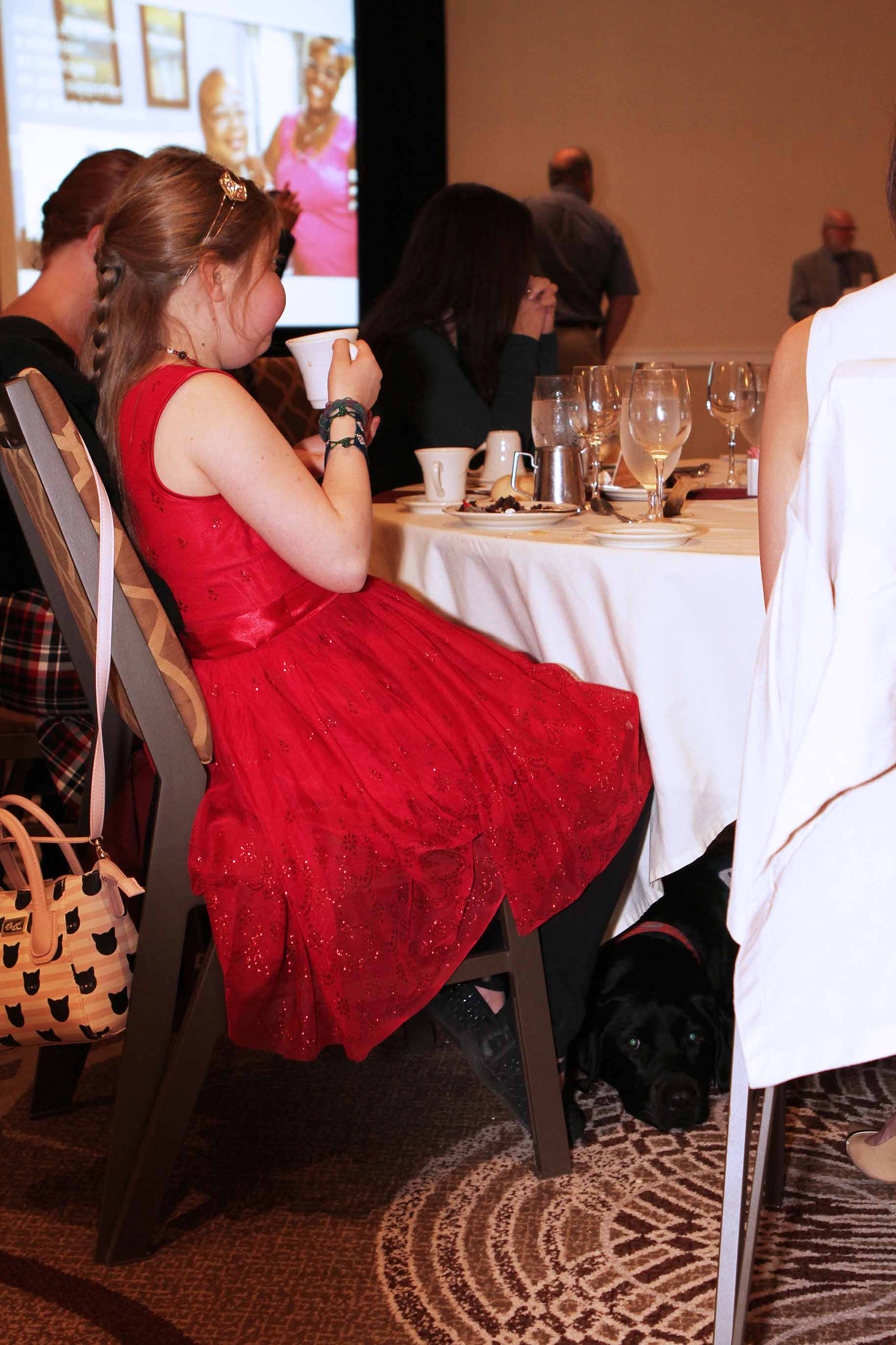 Service dog lays under table at owner's feet while owner dines at a formal event